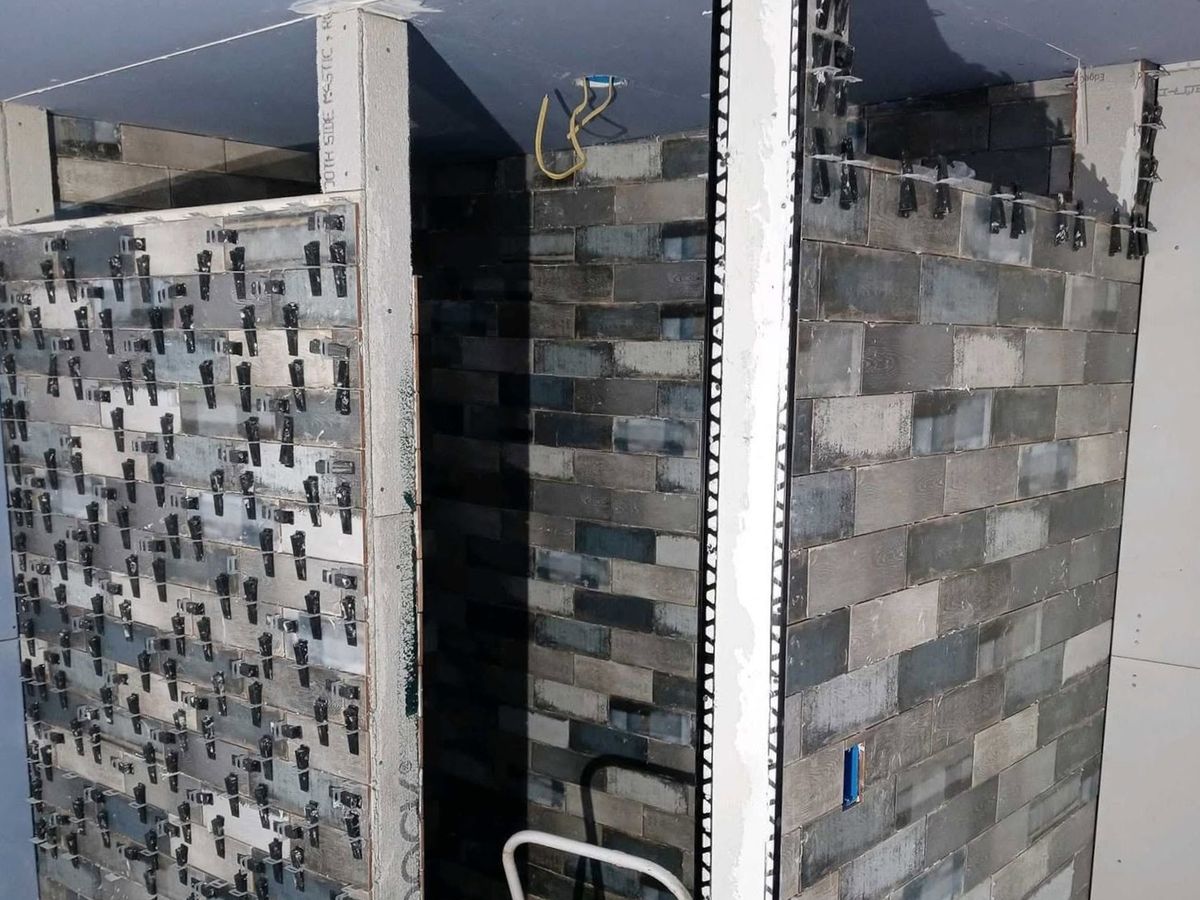 Walk-in shower being tiled with gray and blue weathered-wood-look plank tiles in a running bond on three walls