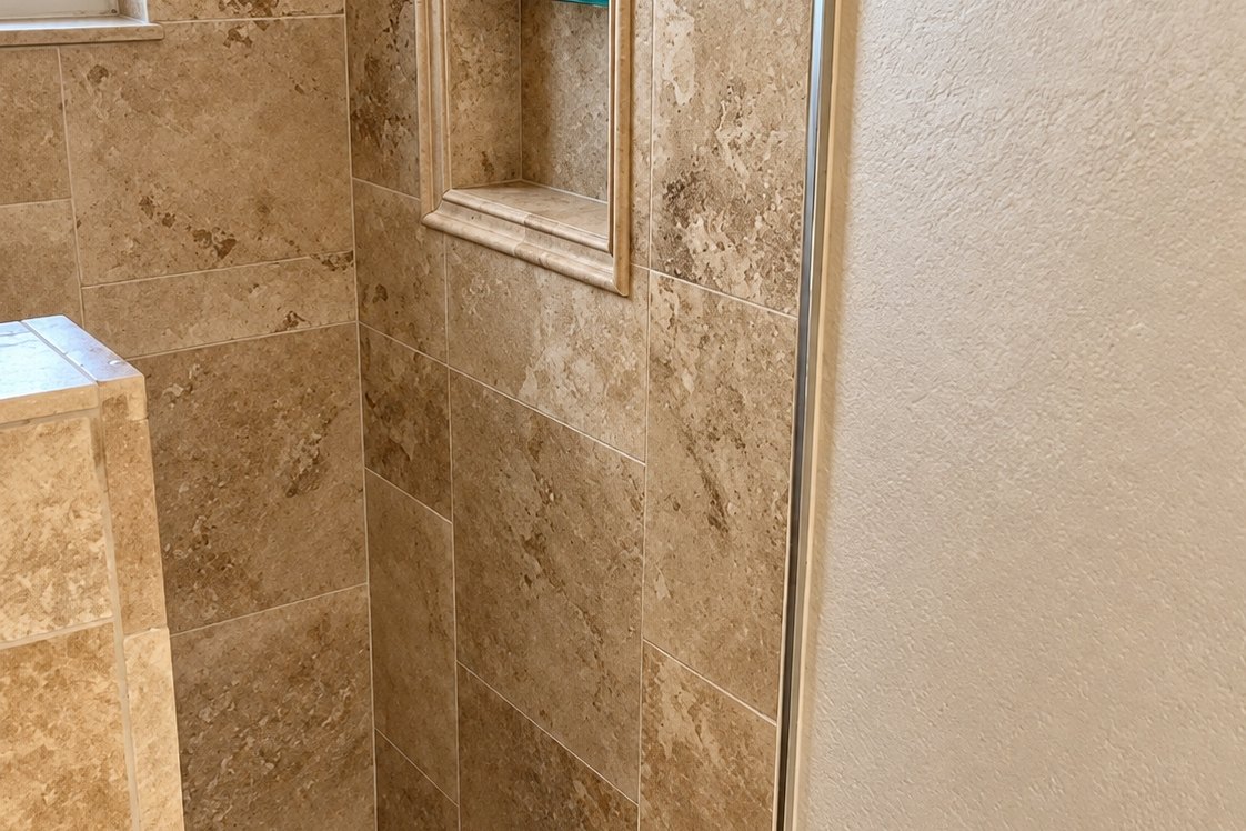 Walk-in shower walled in large tan travertine tile with a recessed niche