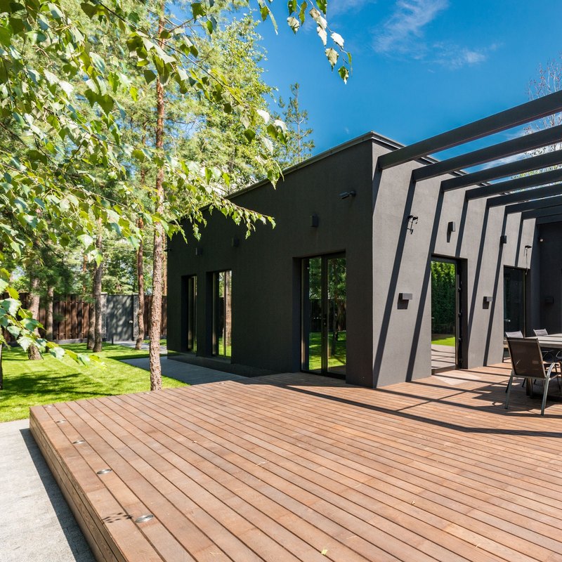Low reddish-brown wood platform deck around a modern dark gray house