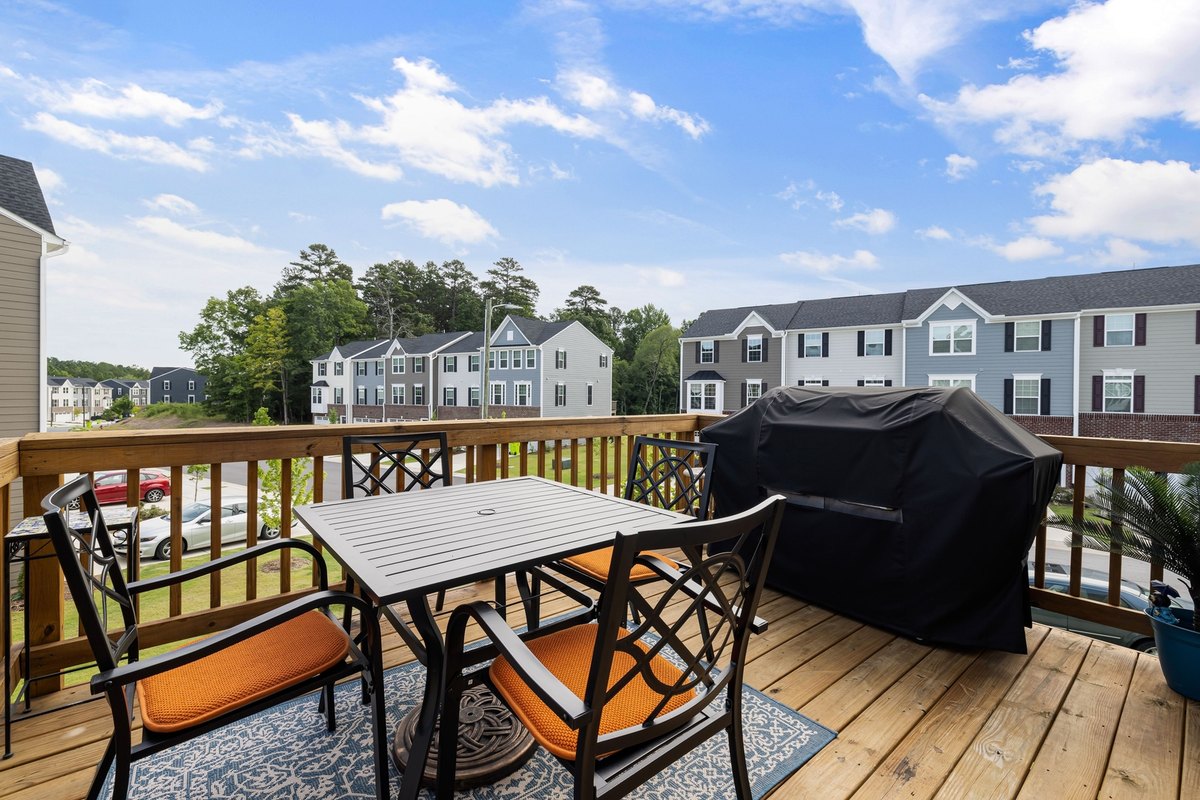 Second-story wood deck with railings, a table, and a covered grill
