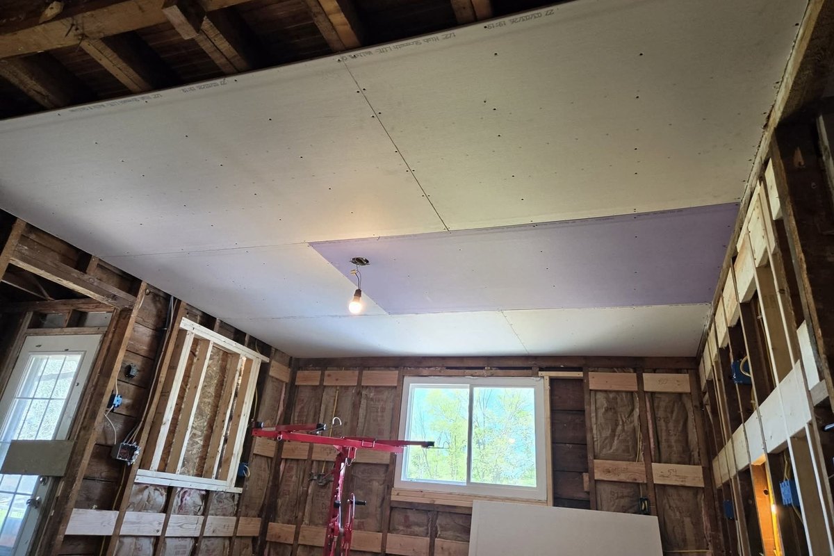 Gutted room with a new drywall ceiling hung in large sheets and a lavender patch panel