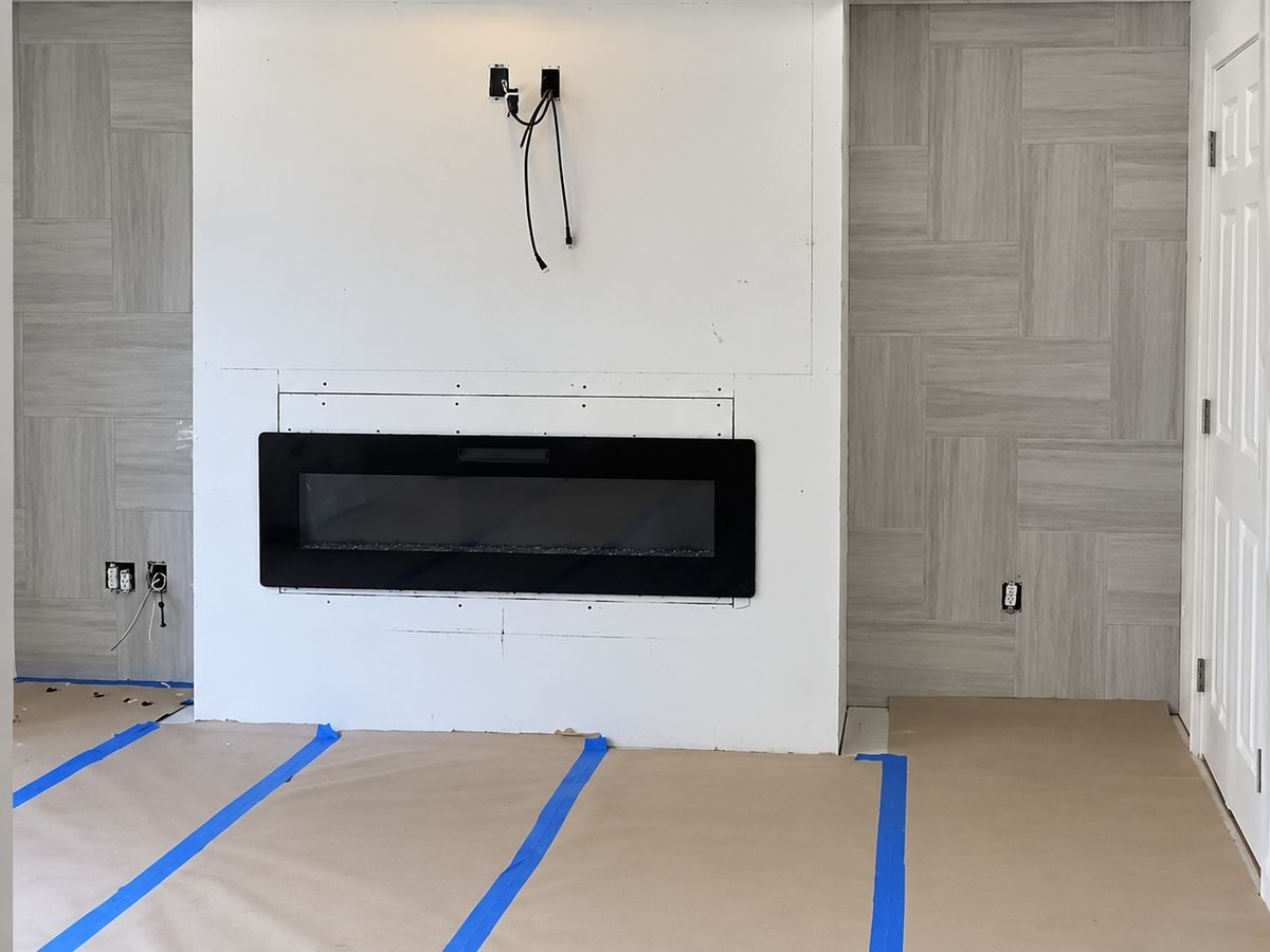 Living-room feature wall in progress: a white drywall chase with a recessed linear electric fireplace and TV wires