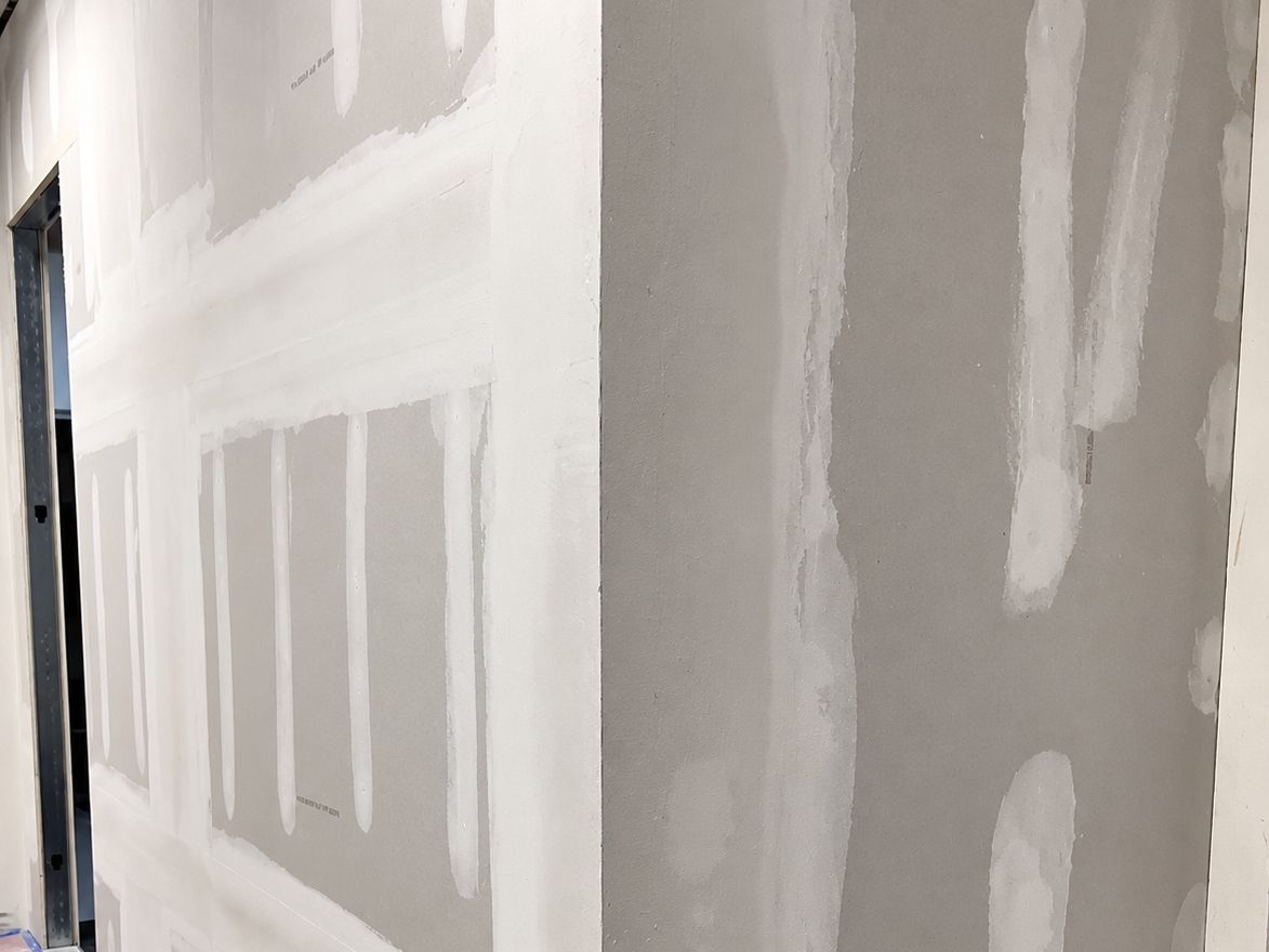 Hallway with new drywall taped and covered in patches of joint compound beside an open doorway