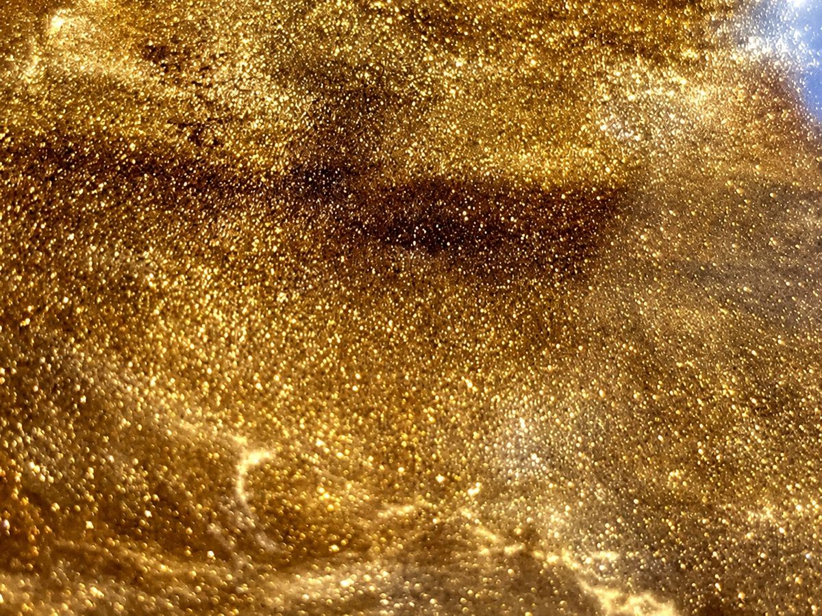 Extreme close-up of a metallic gold epoxy surface full of glittering pigment swirled into darker bronze clouds
