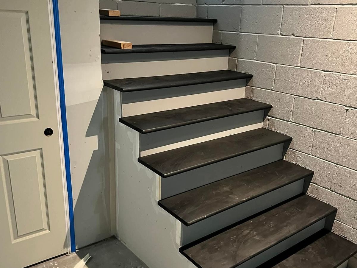 Finished basement stairs with white painted risers and dark gray plank treads turning around a corner