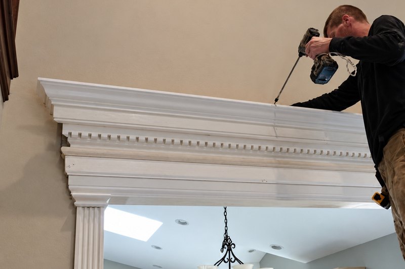 Carpenter leaning over a tall white dentil header above a wide opening