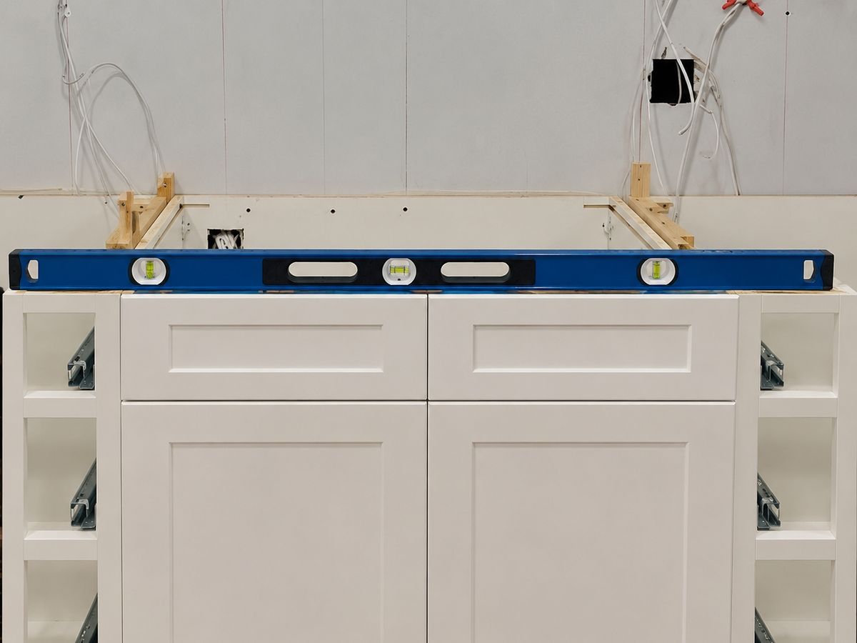 Kitchen sink base: a white shaker sink base cabinet flanked by open narrow cabinets showing drawer slides