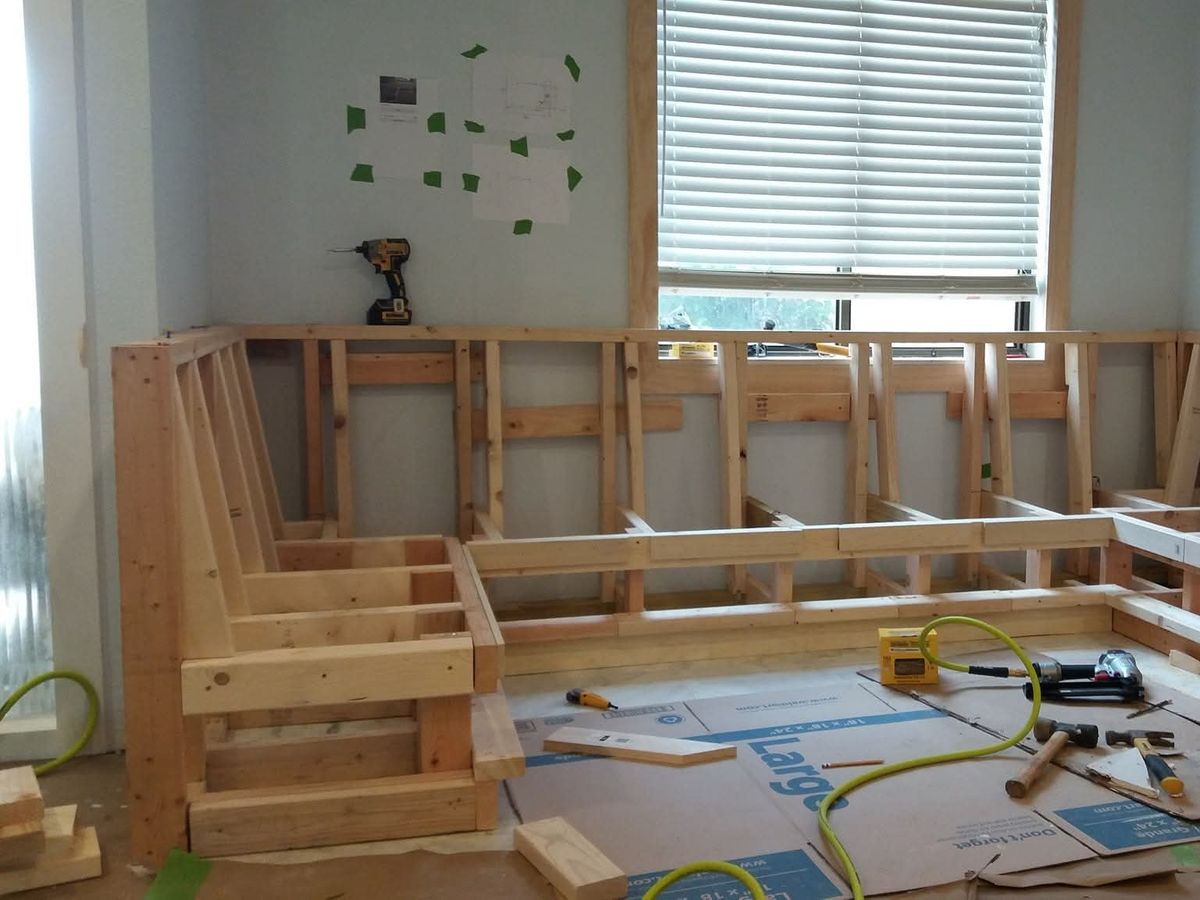 Wood-framed L-shaped bench seat built from 2x4 lumber along two walls under a window