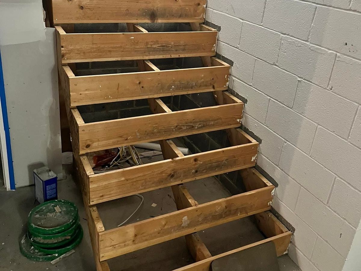 Basement staircase framed in rough lumber with open boxes for each step against a white block wall