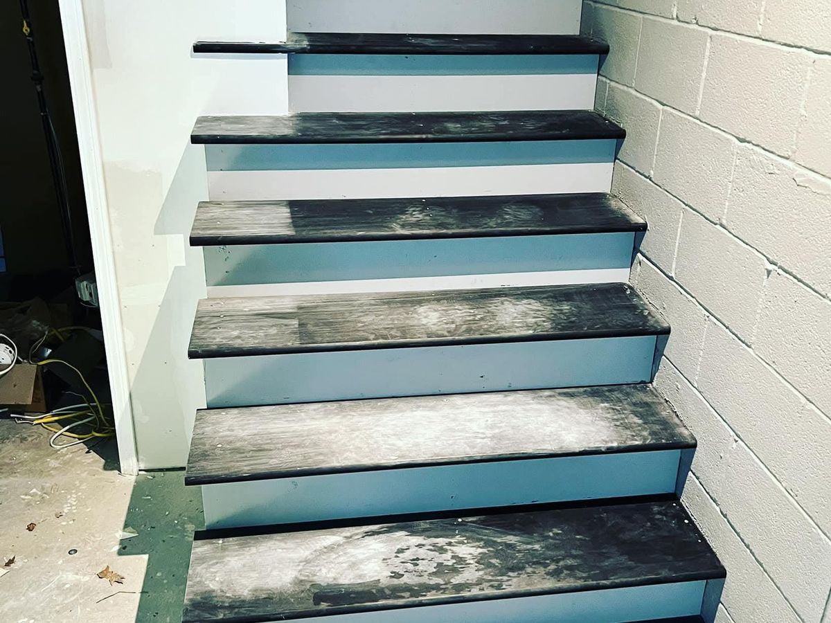 Narrow basement staircase with dark gray treads dusty from sanding