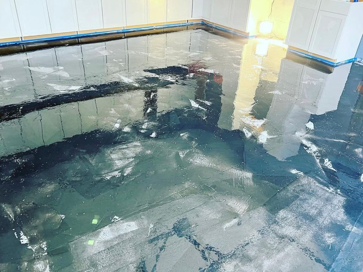 Wet-looking blue, teal and black metallic epoxy floor with white streaks reflecting white cabinets
