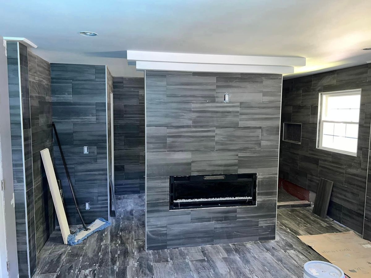 Room tiled in dark gray wood-grain porcelain on the floor and walls, with a linear electric fireplace in a tiled chase