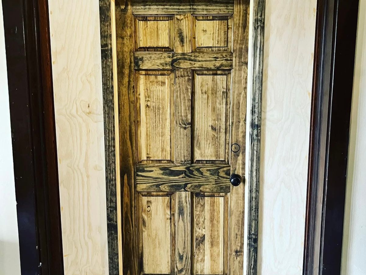 Rustic six-panel wood door with a dark stained edge in a dark wood frame, with fresh plywood filler panels