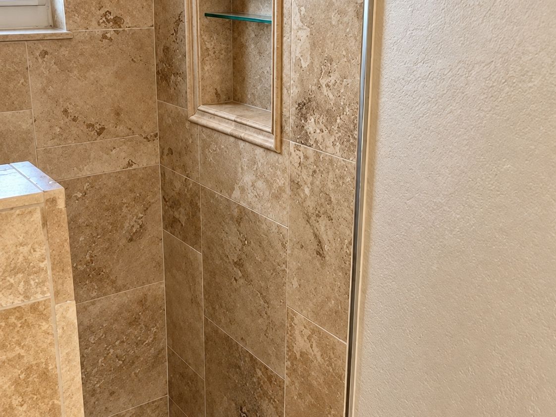 Finished shower with large tan travertine tile and a niche holding a glass shelf