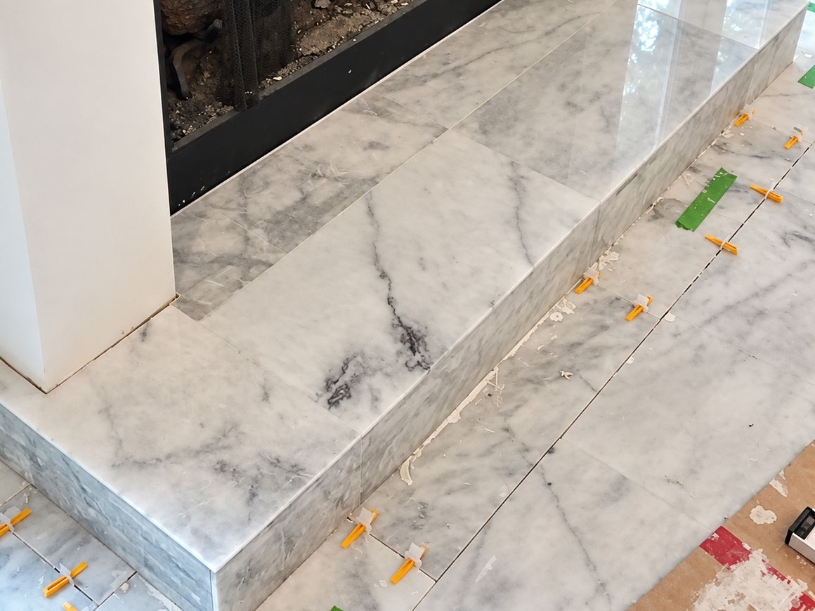 Fireplace with a black surround and a raised white and gray marbled tile hearth with a stepped front
