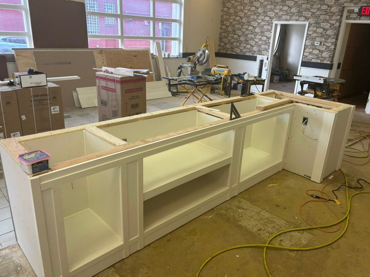 Long white custom cabinet base unit with open shelf bays and a raw wood top being built in a storefront