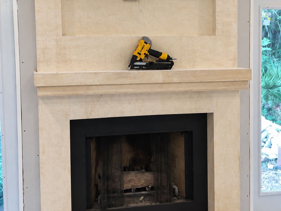 Tall cream stone-look fireplace surround with a black firebox and stepped hearth over marble floor tile