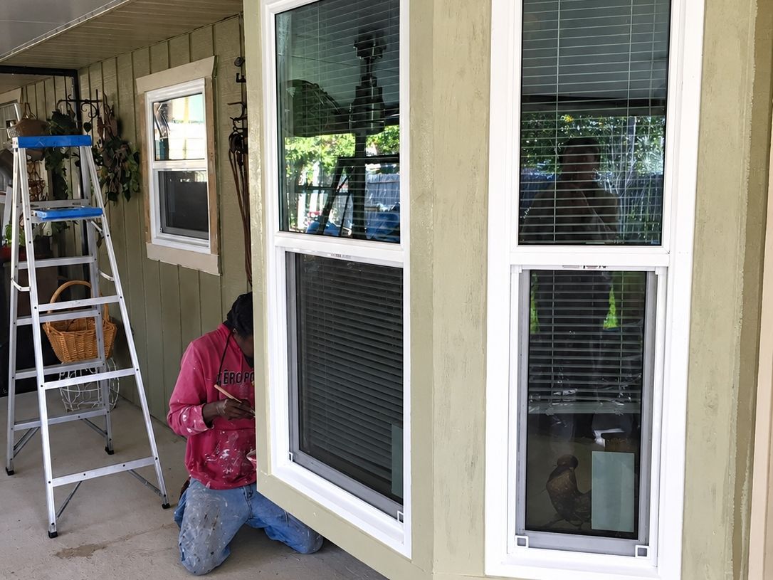 Bay window with three white sashes and white trim installed in green siding under a porch ceiling