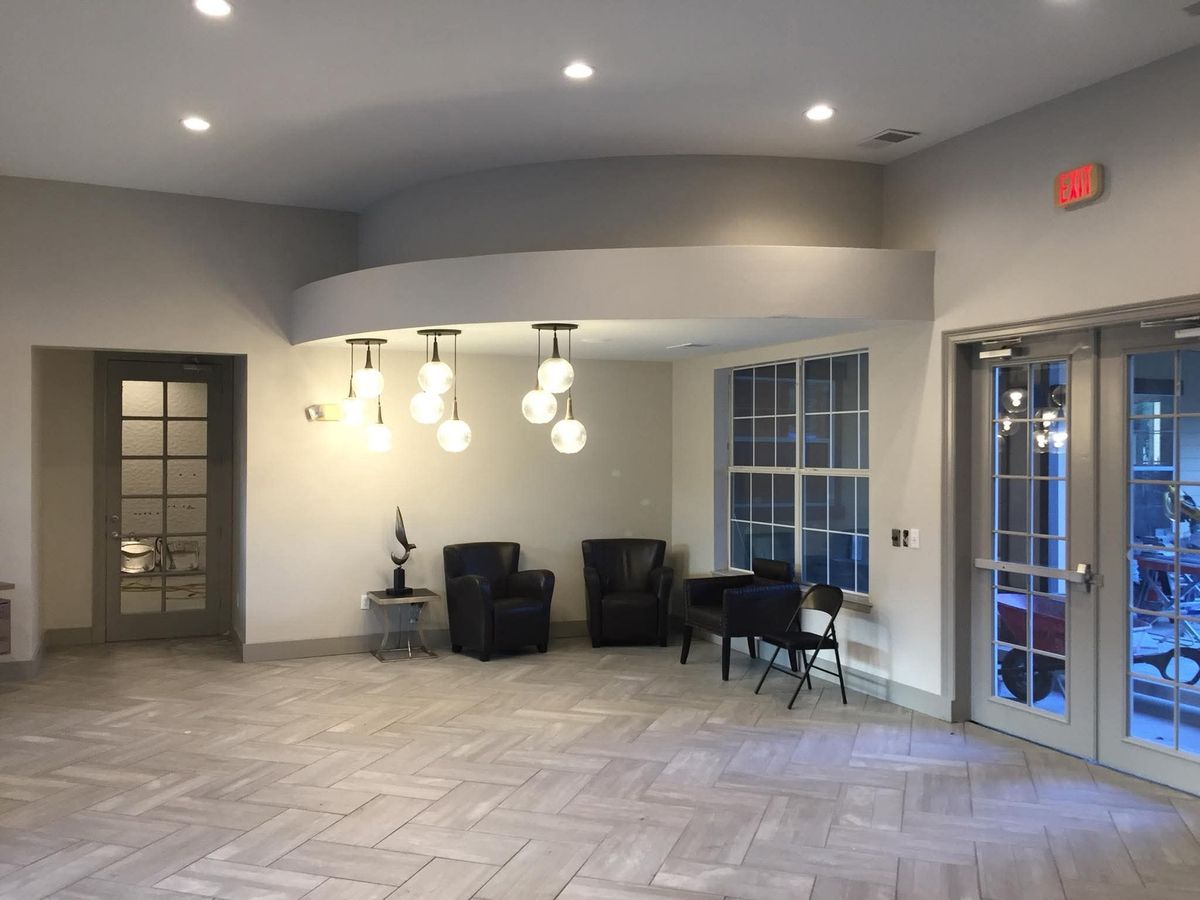 Open lobby with herringbone gray porcelain floor tile, a curved soffit, pendant globe lights, and armchairs by french doors