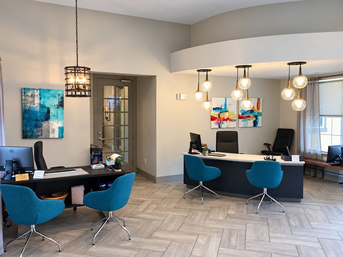 Reception lobby with herringbone gray tile floor, curved soffit with globe pendant lights, a curved desk, and teal chairs