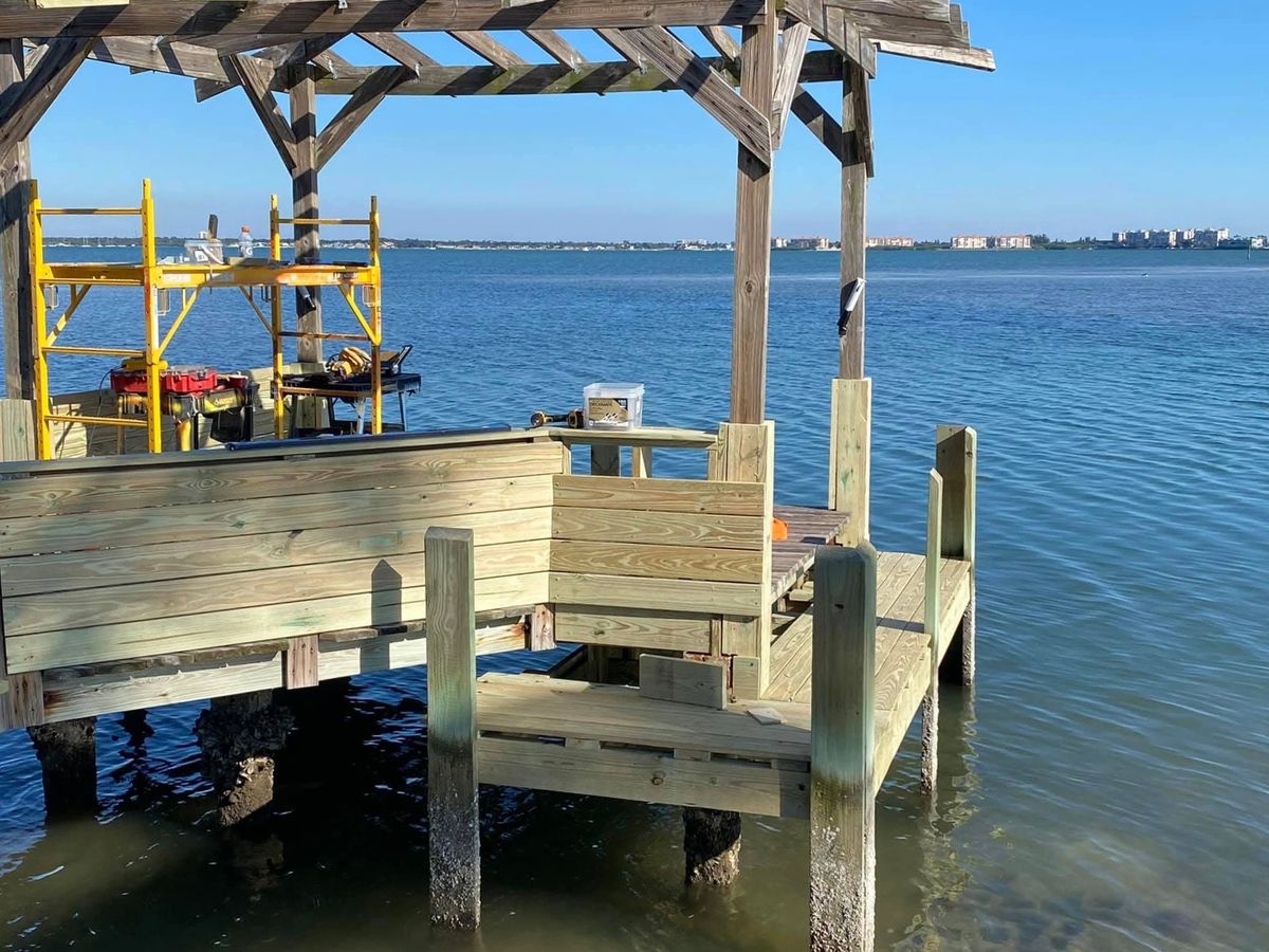 Pier platform with a wood-roofed gazebo, a built-in bench along the rail, yellow scaffold and tools