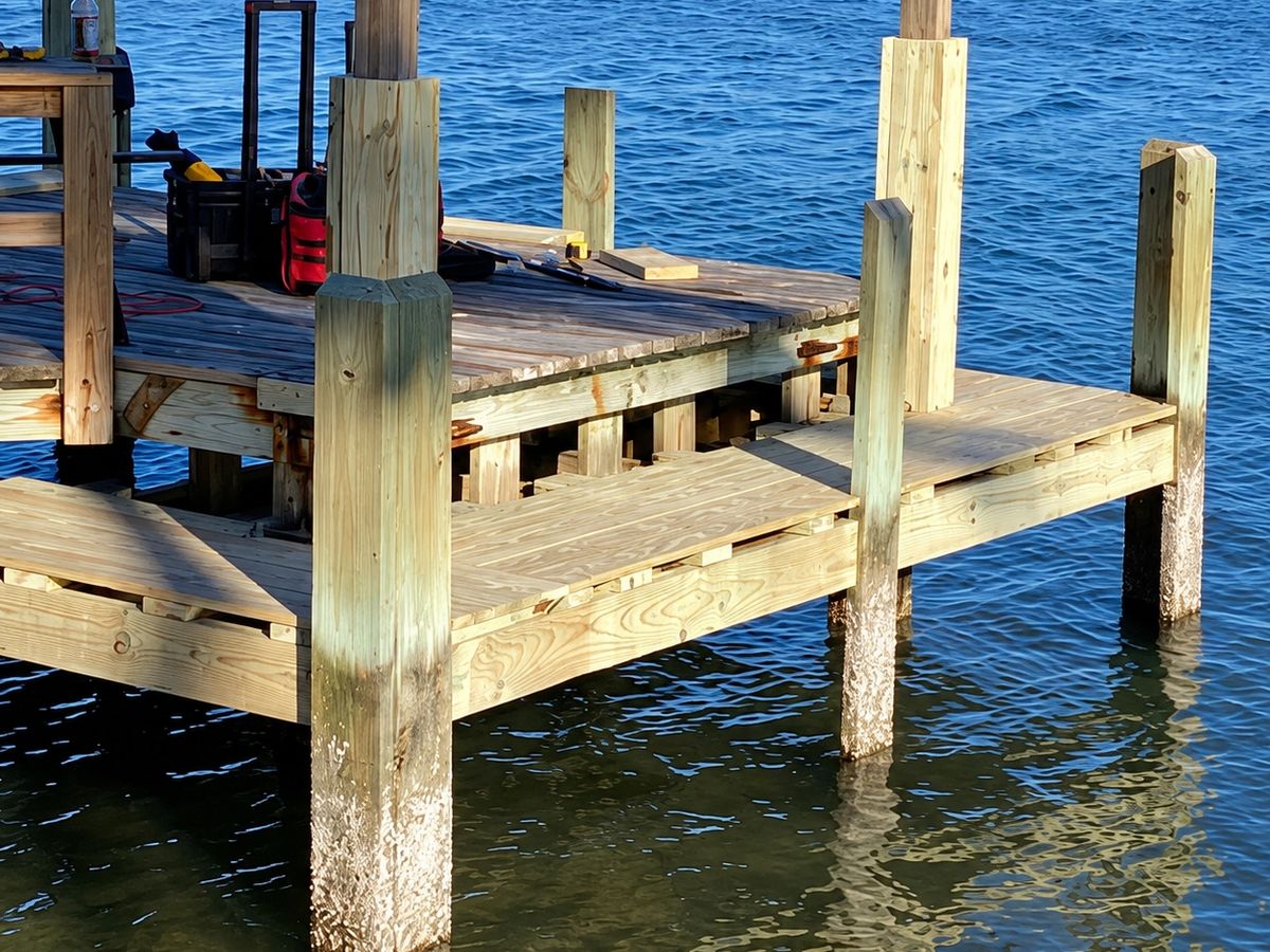 Corner of a new pressure-treated wood pier platform with square posts and stairs over blue water