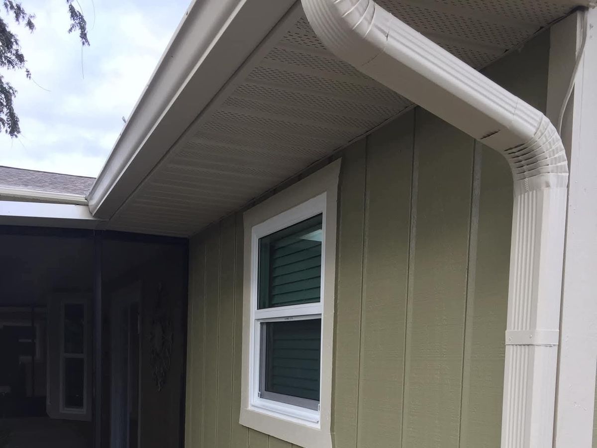 Finished white-framed double-hung window with grilles in green board-and-batten siding beside a white gutter downspout