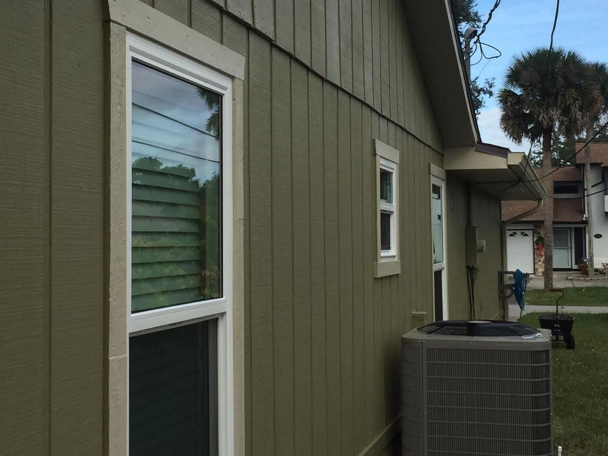 Side of a green board-and-batten house with a new white double-hung window with grilles, a gutter