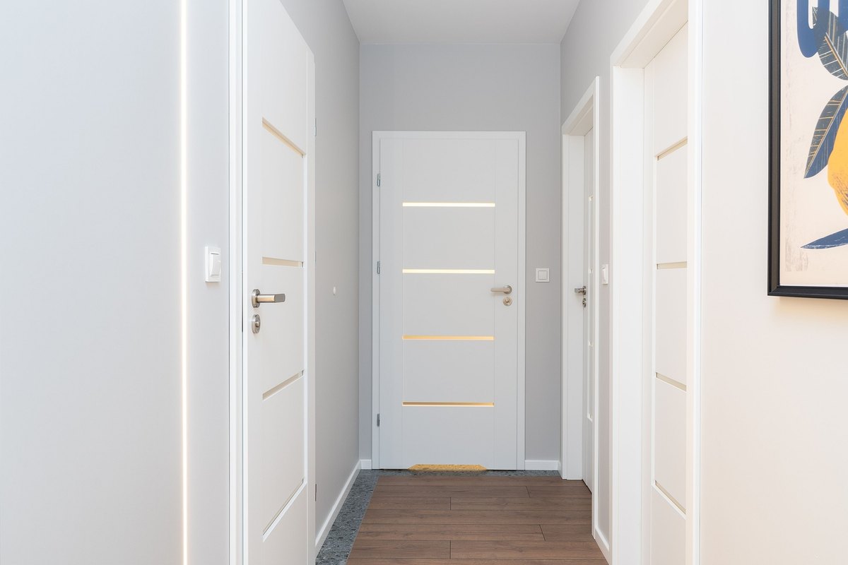 Bright hallway lined with white interior doors with brushed steel handles and a white door at the end