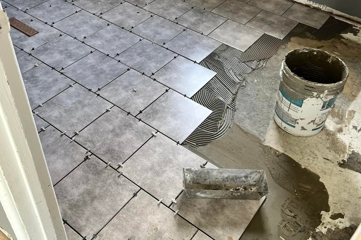 Large square gray porcelain floor tiles being set in thinset with spacers