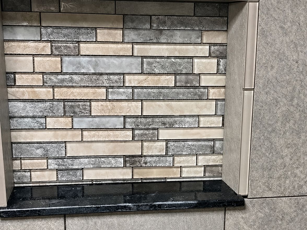 Close-up of a tiled bathroom shower niche: a mosaic of glass and stone linear strips in gray and beige inside the niche
