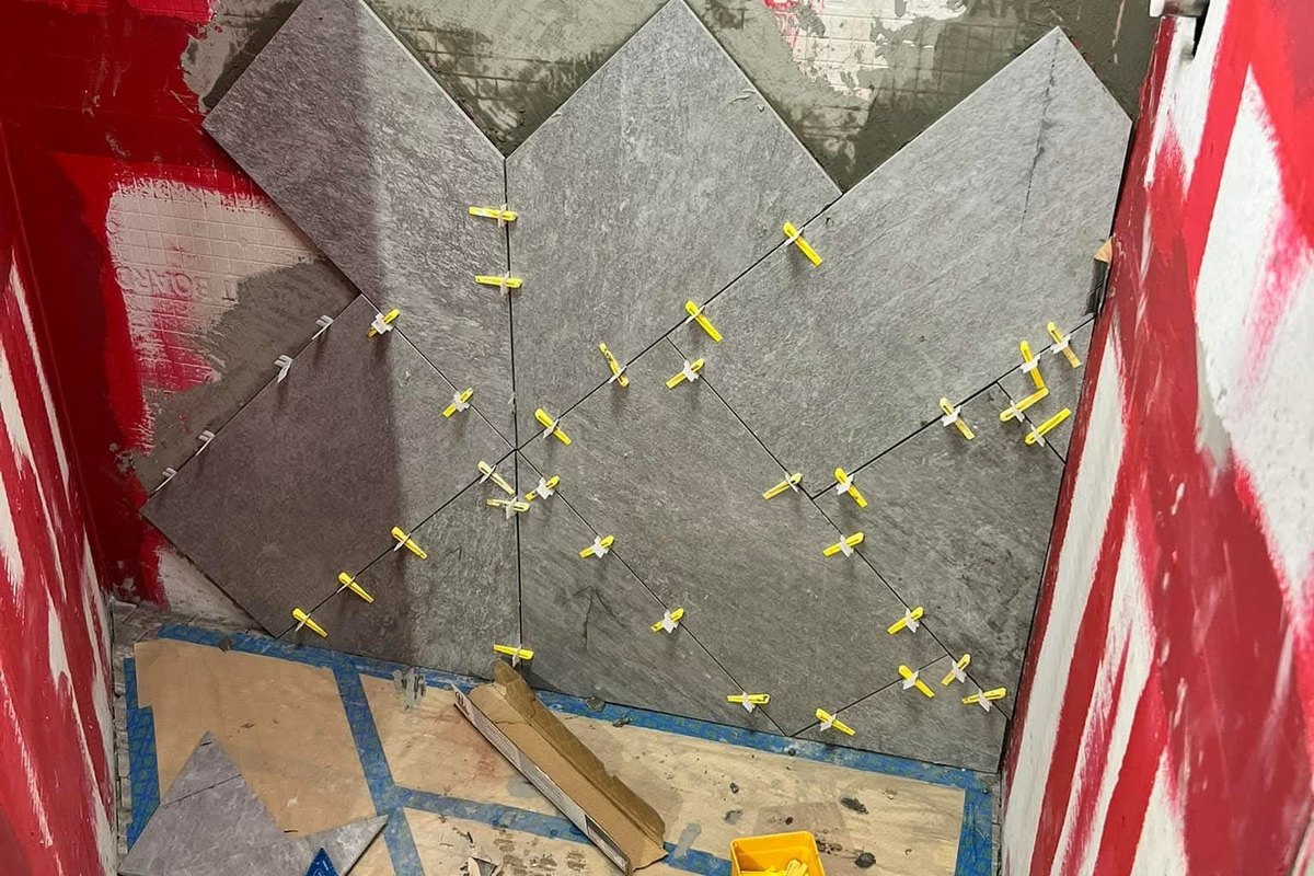 Shower alcove with large dark gray tiles set in a chevron pattern and yellow leveling clips