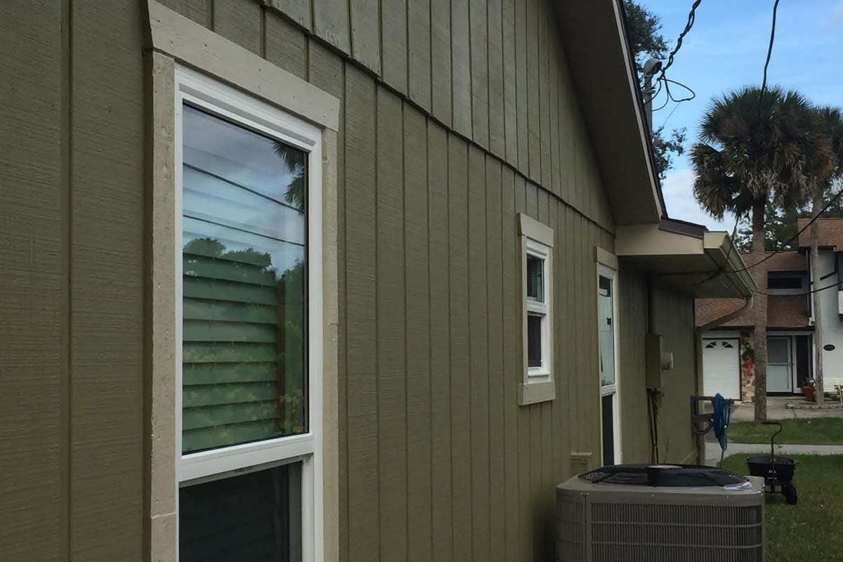 New white double-hung window in green board-and-batten siding beside a gutter